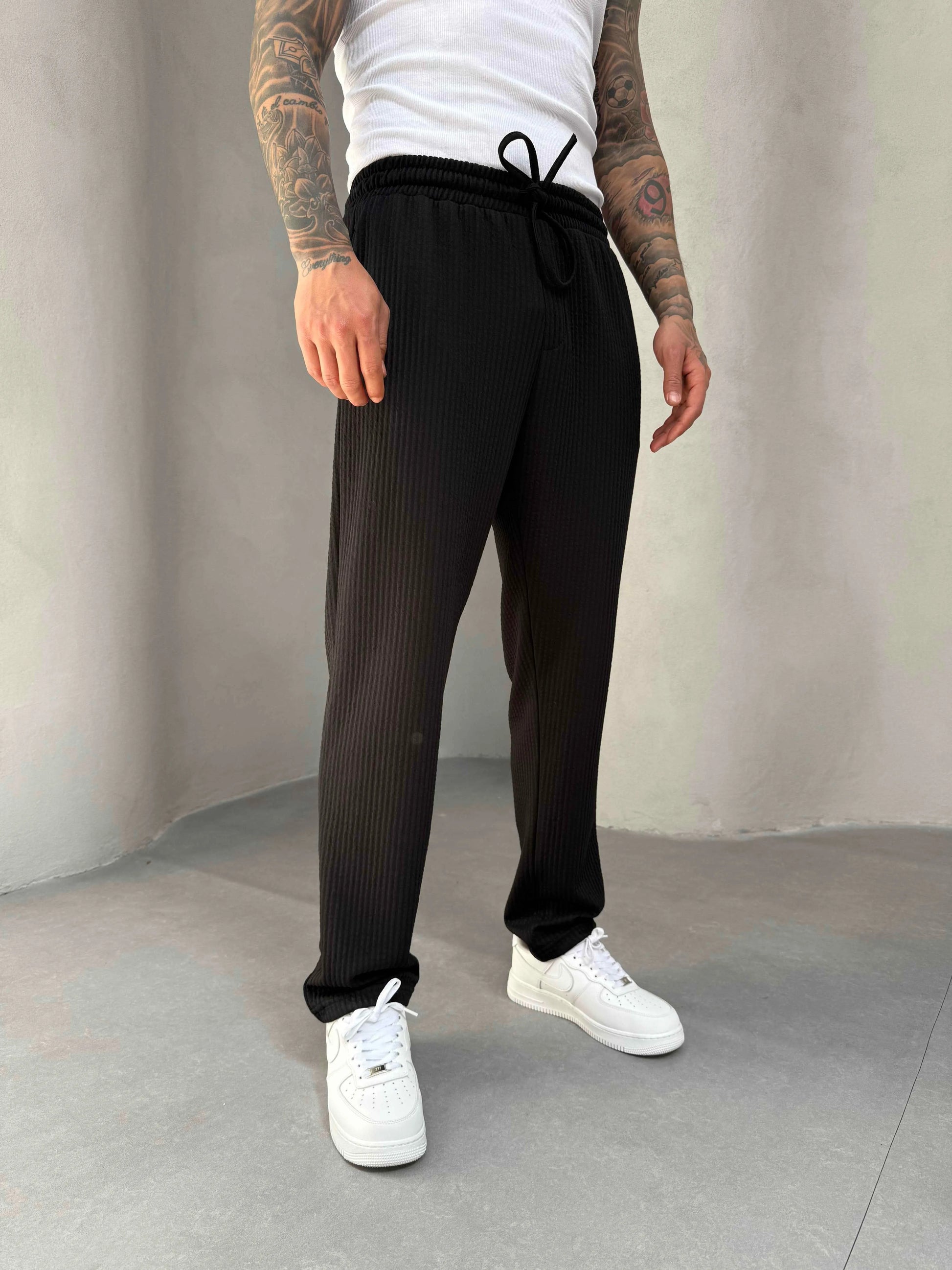 Person wearing black ribbed knit jogger pants and white sneakers on a plain background