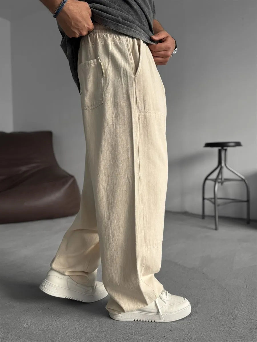 Person wearing beige linen pants and white shoes in a minimalistic setting