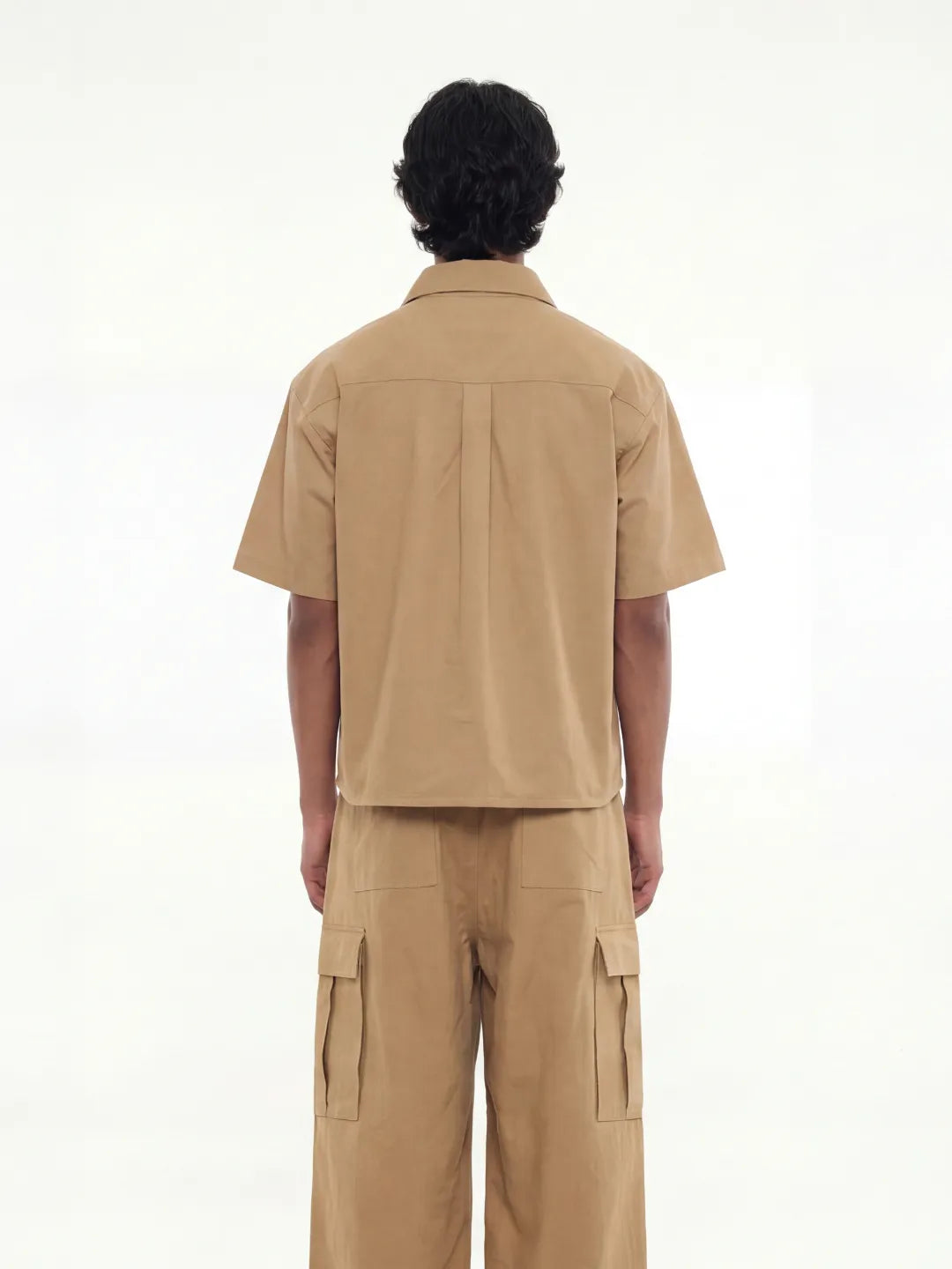 Person wearing a beige outfit with a shirt and cargo pants on a white background