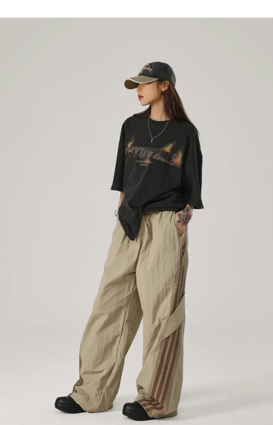 Person wearing a black oversized shirt, beige pants, and a cap on a plain background