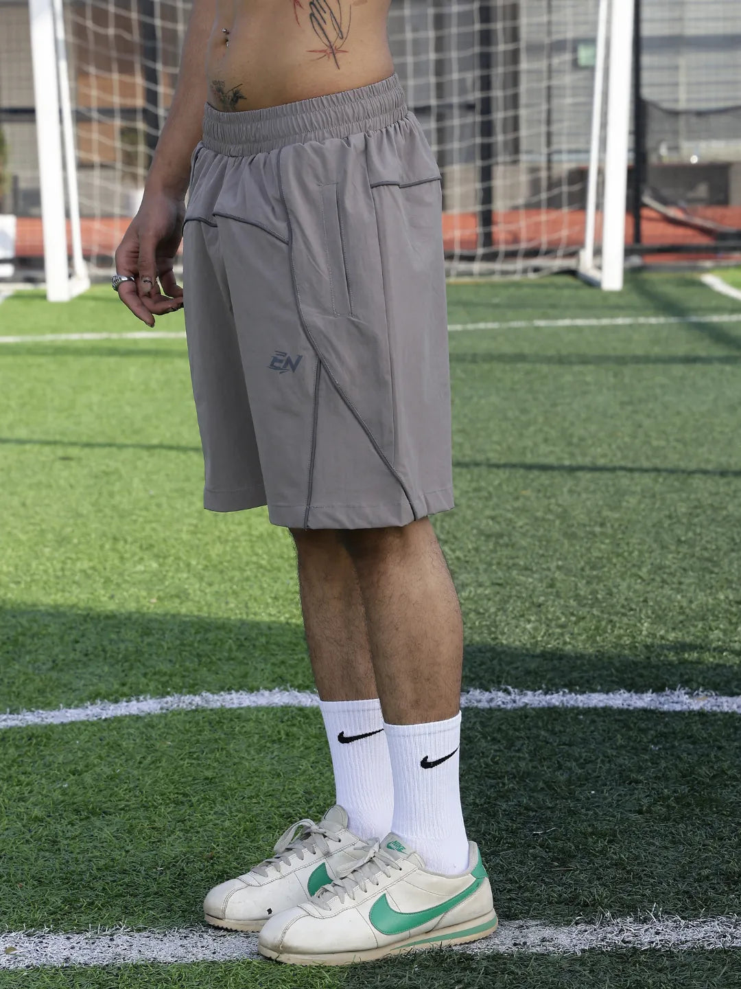 Person wearing grey shorts and white sneakers with green accents on a sports field.