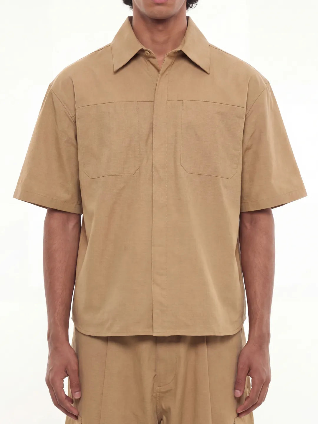 Man wearing a beige short-sleeve shirt and pants on a white background