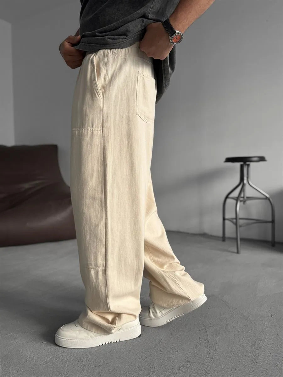 Person wearing beige linen pants and white shoes in a minimalistic room.