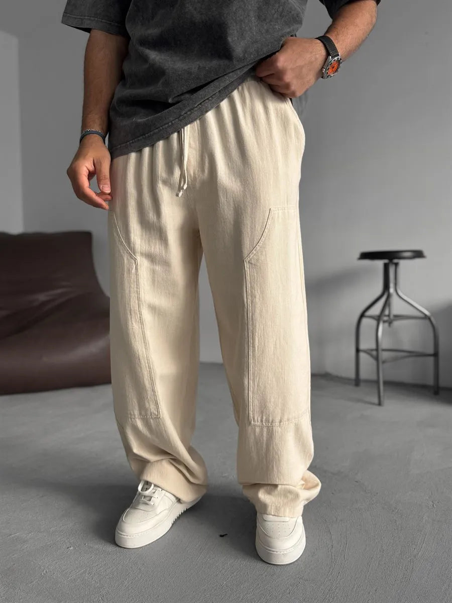 Person wearing beige linen pants and white shoes in a minimalistic setting