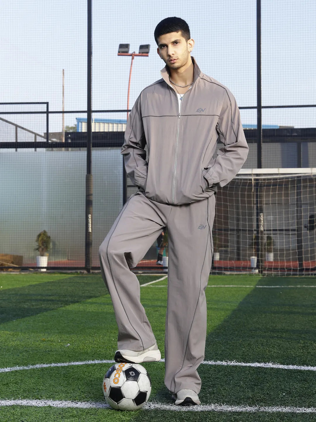 Man in grey tracksuit standing on a soccer field with a soccer ball