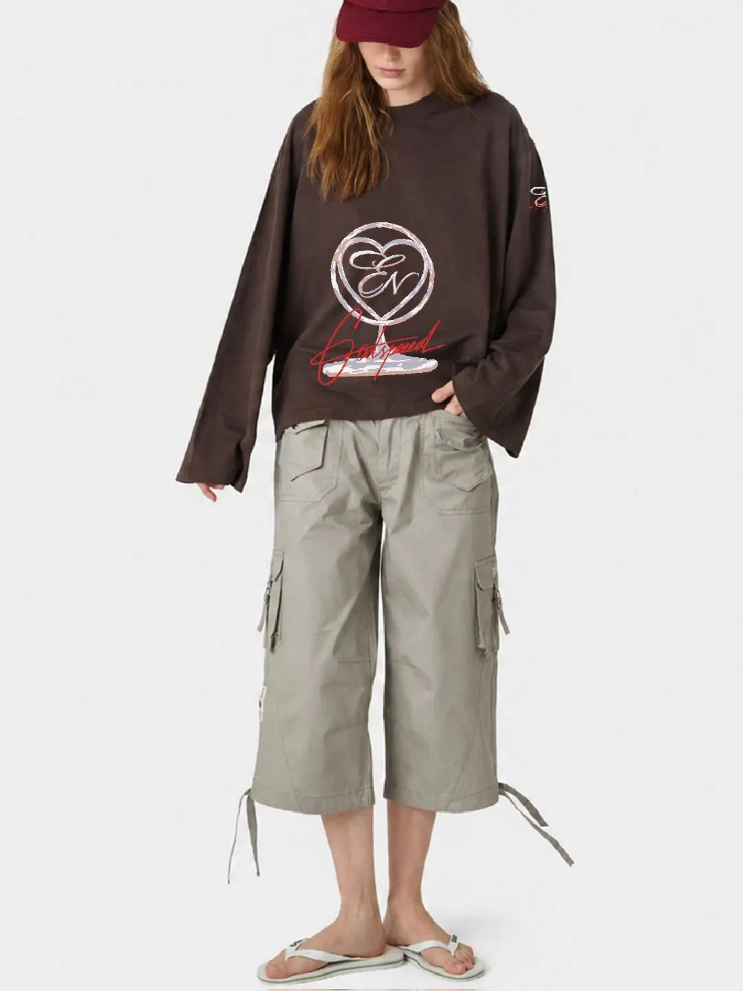 Person wearing a brown full sleeve oversized t-shirt with a logo and beige cargo pants on a white background