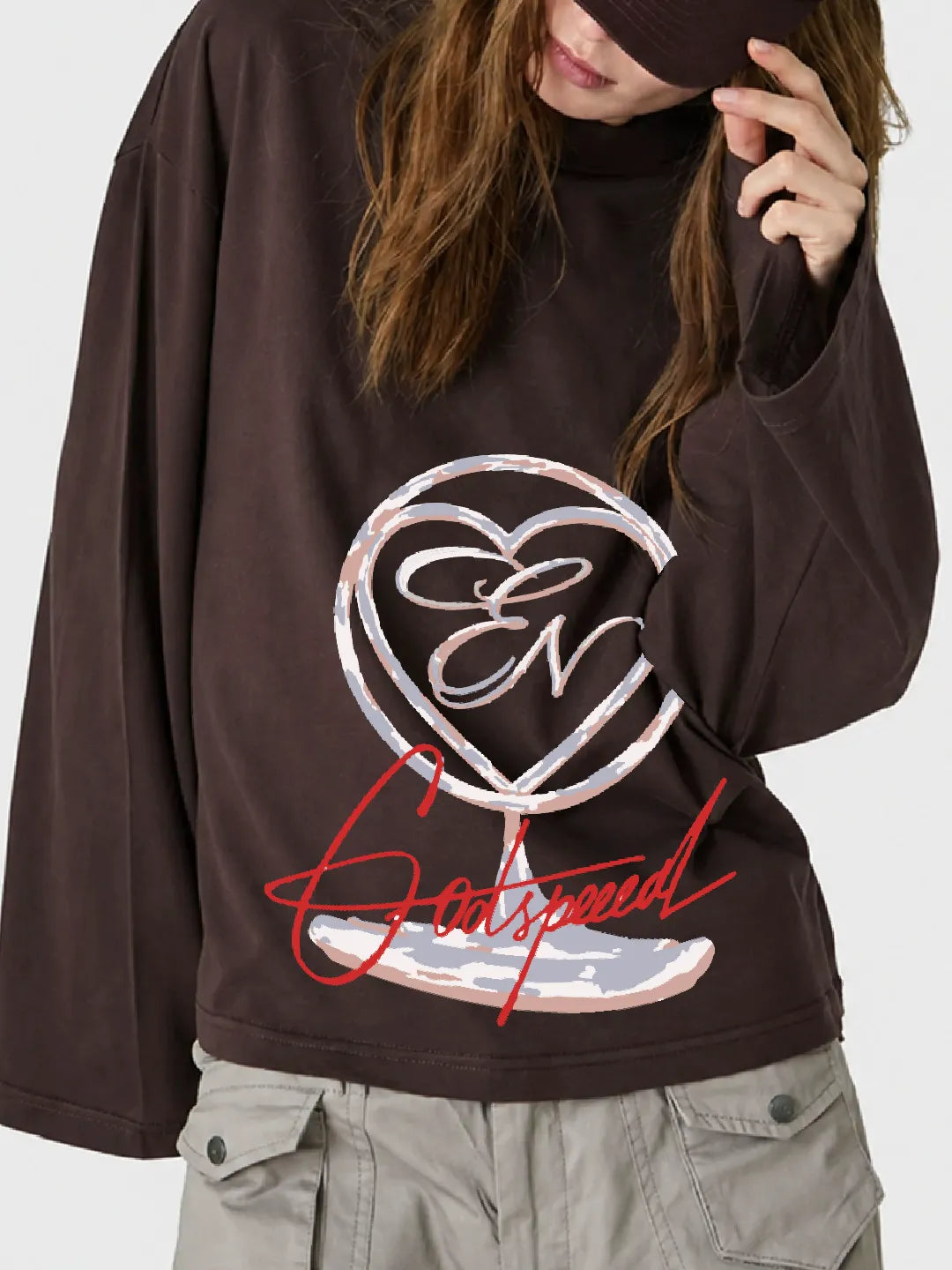 Person wearing a brown long-sleeve oversized t-shirt with a logo and text on a plain background