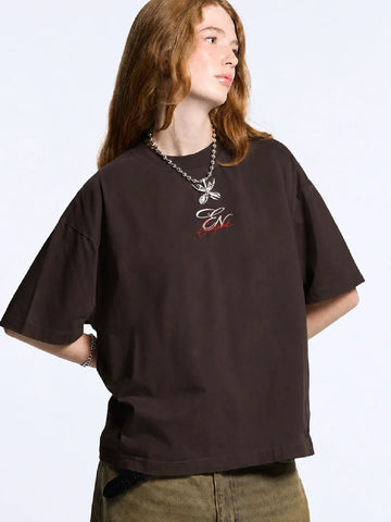 Person wearing a dark brown oversized t-shirt with a logo on a plain background