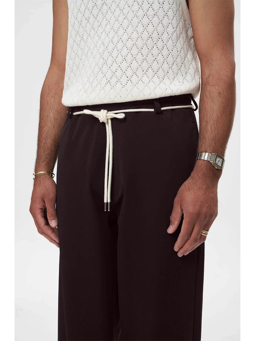 Person wearing a white textured top and brown trouser pants with a drawstring on a white background