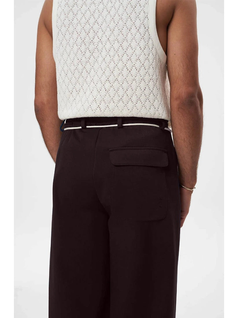 Person wearing a white textured sleeveless top and brown pants on a white background