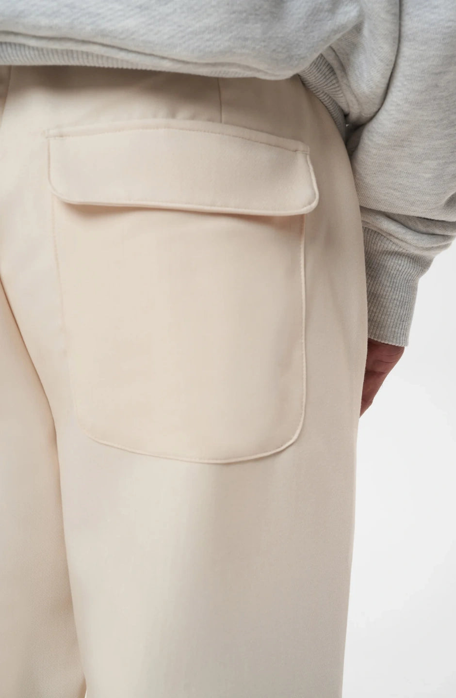 Beige pants with a pocket detail worn by a person, on a plain background