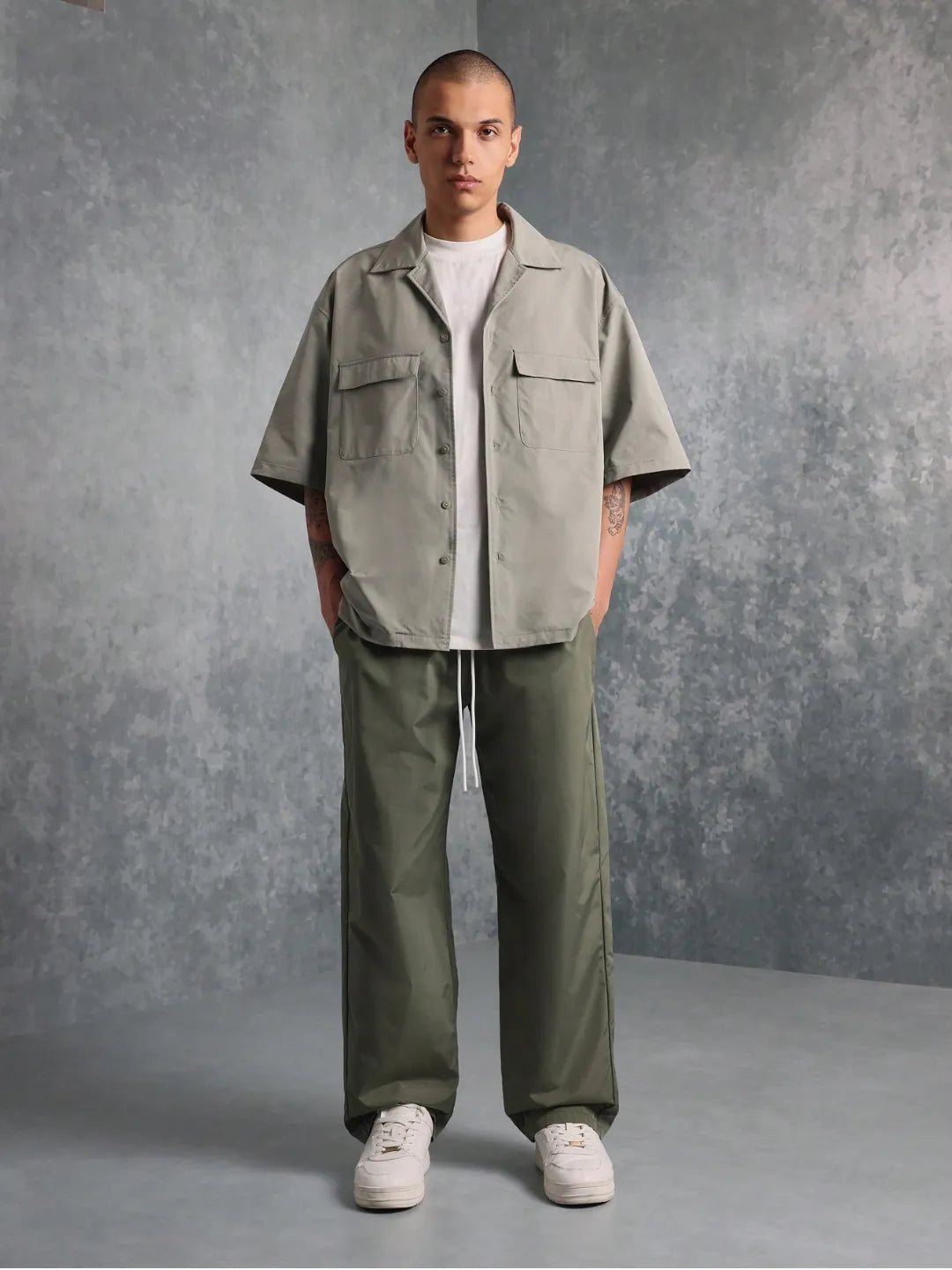 Man wearing a light green shirt and dark green pants against a grey background