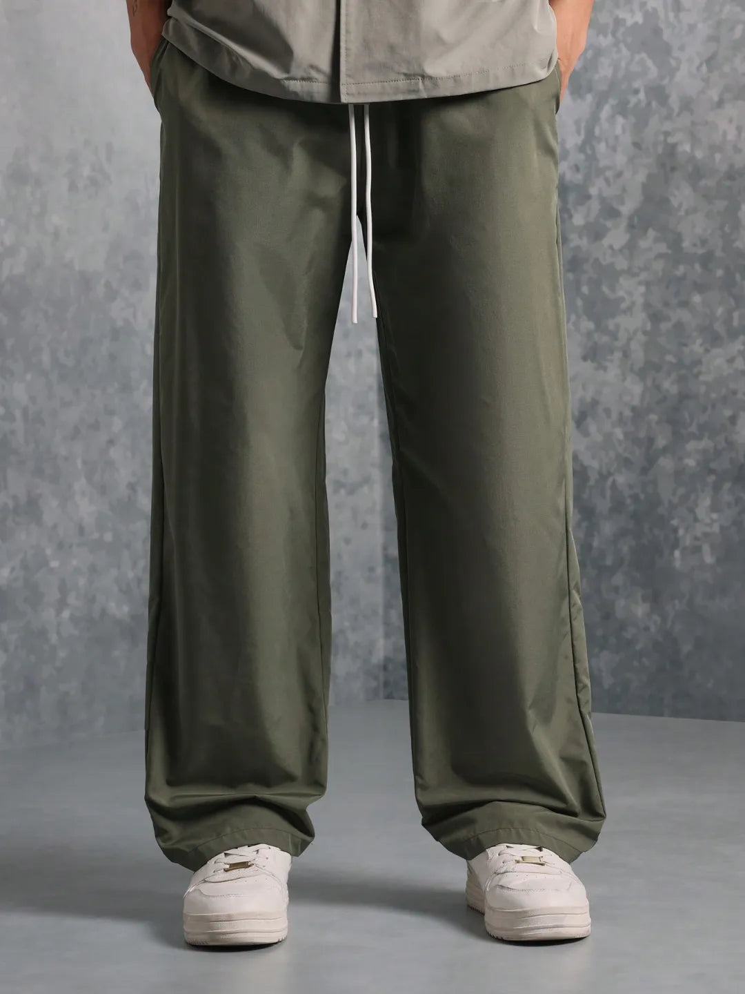 Person wearing olive green pants and white sneakers on a grey background