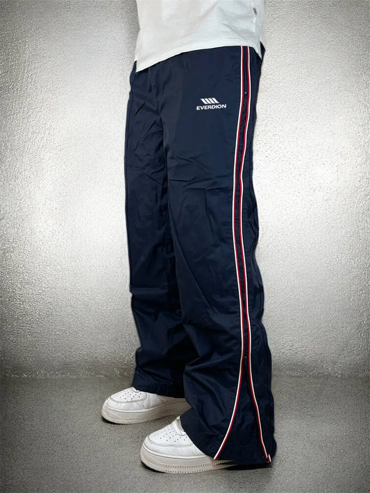 Navy track pants with a red stripe and brand logo on a grey background
