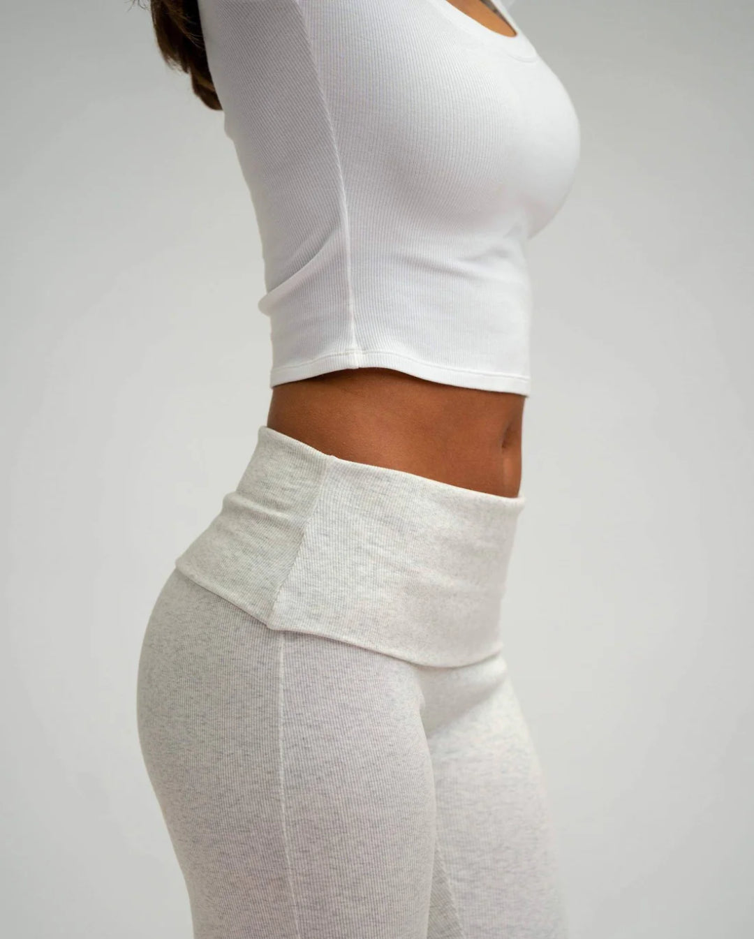Person wearing a white long-sleeve top and grey leggings on a plain background