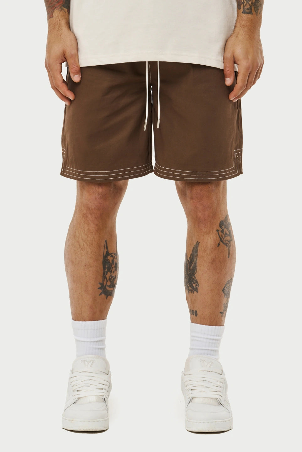 Person wearing brown shorts with white accents on a plain background