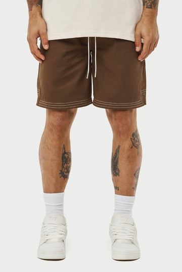 Person wearing brown shorts with white accents on a plain background