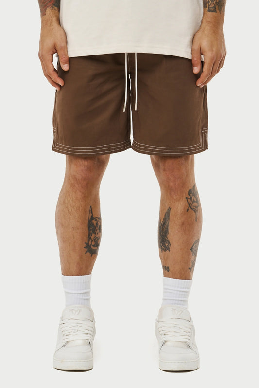 Person wearing brown shorts with white accents on a plain background