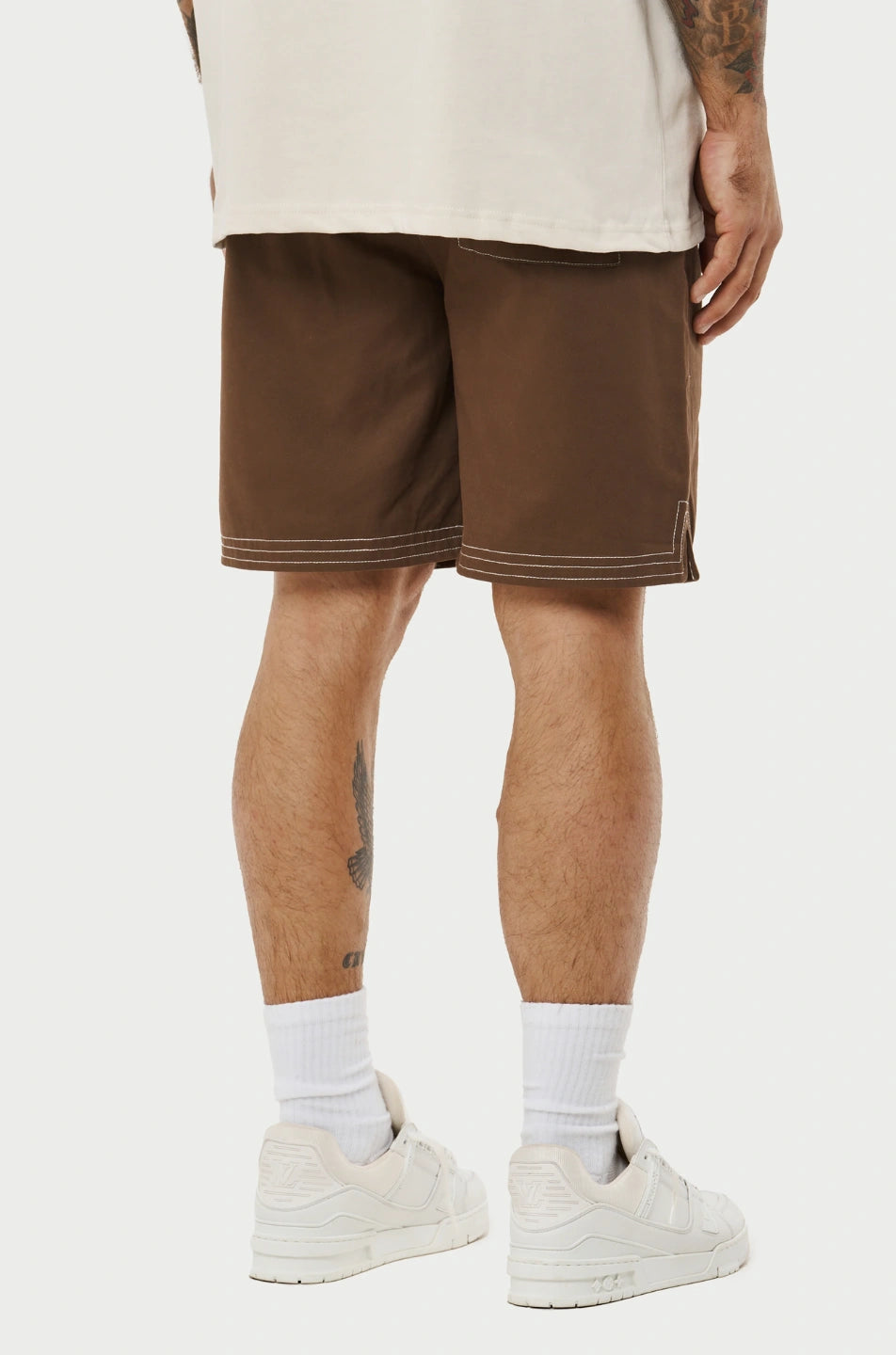 Person wearing brown shorts and white sneakers on a plain background