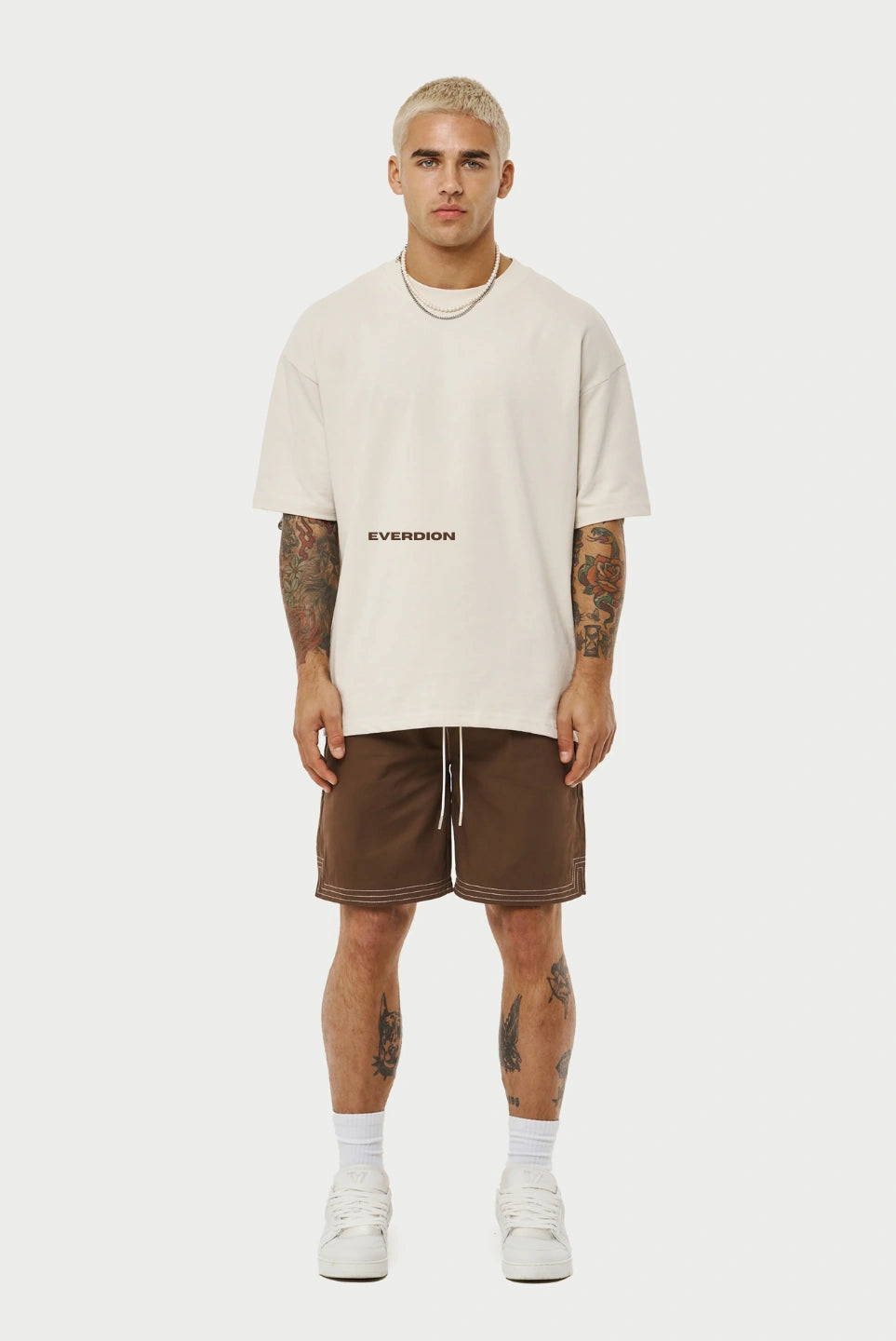 Man wearing a beige t-shirt and brown shorts on a white background