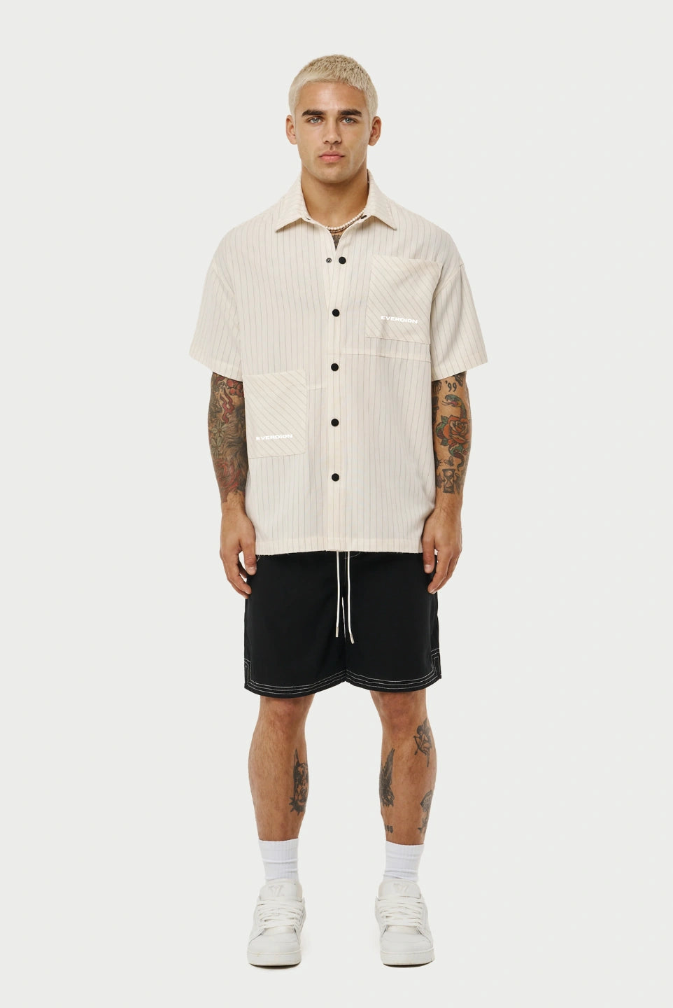 Man wearing a beige short-sleeve shirt and black shorts on a white background