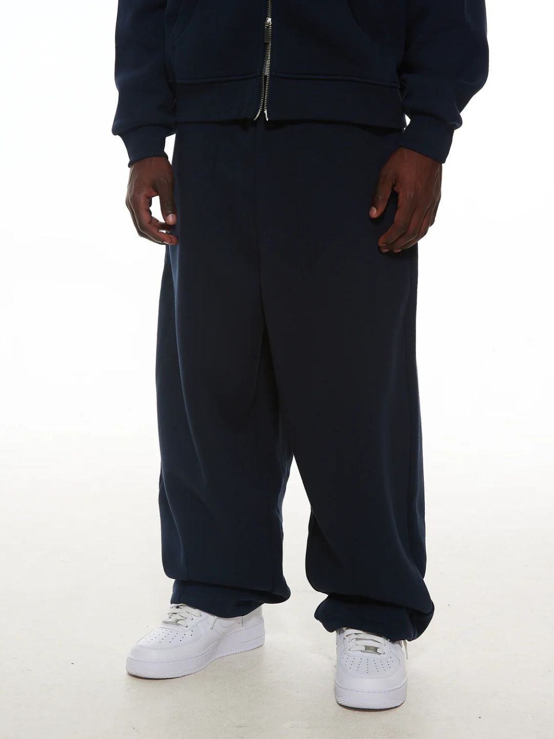 Person wearing navy blue tracksuit with white sneakers on a white background
