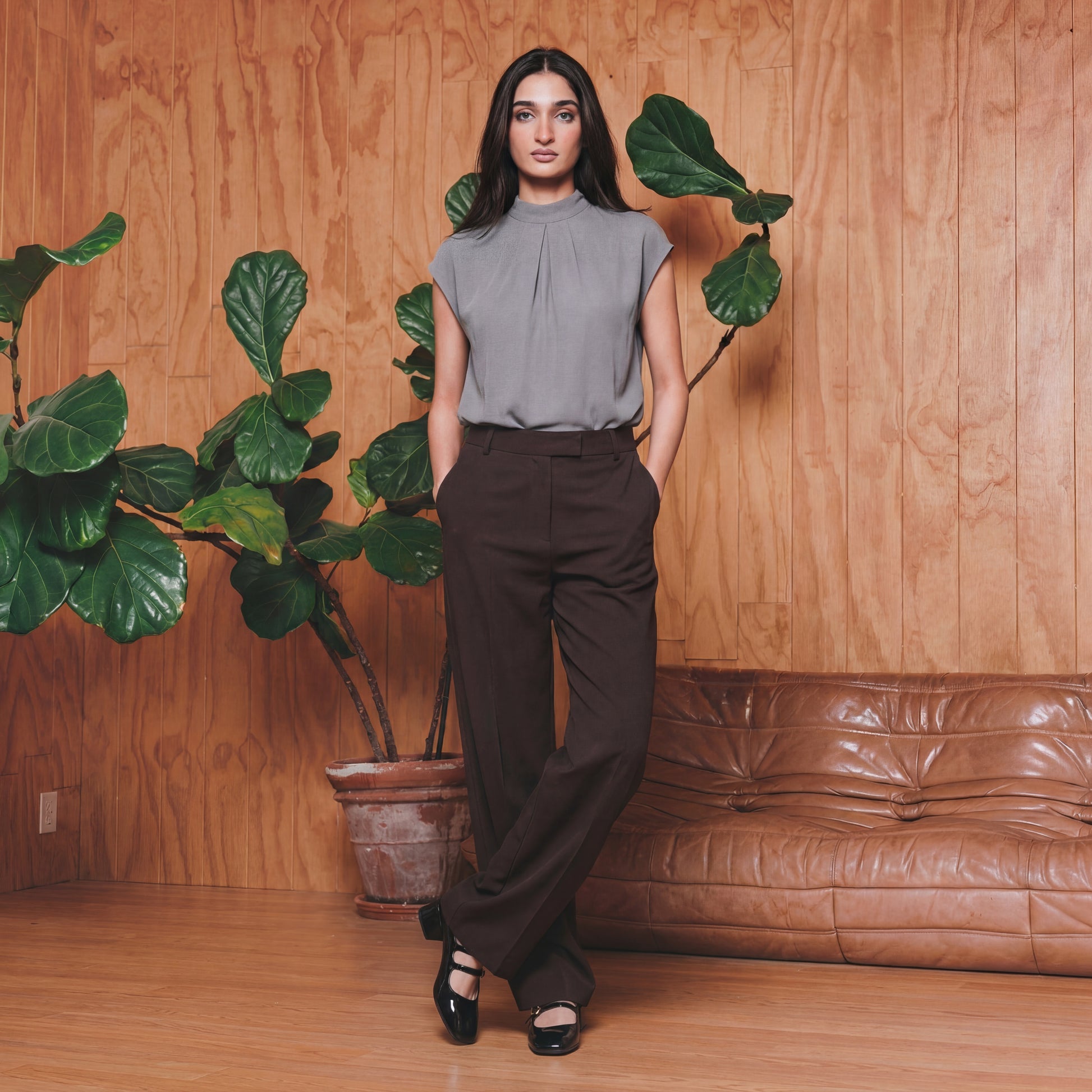 Woman standing in a room with wooden walls, a brown leather couch, and potted plants.