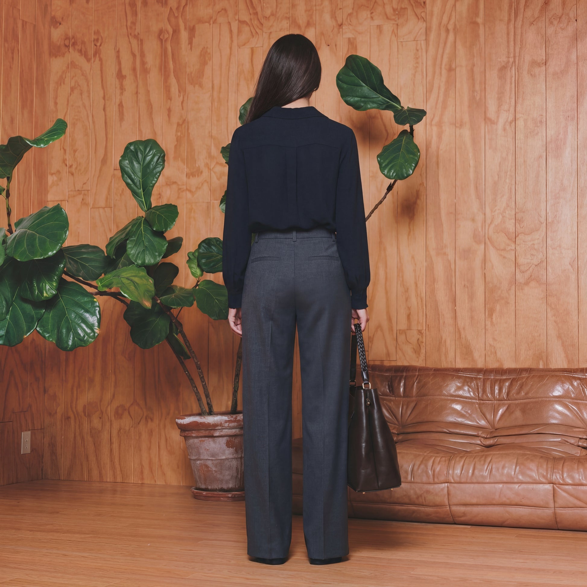 Person standing in a room with wooden walls, plants, and a brown leather couch.