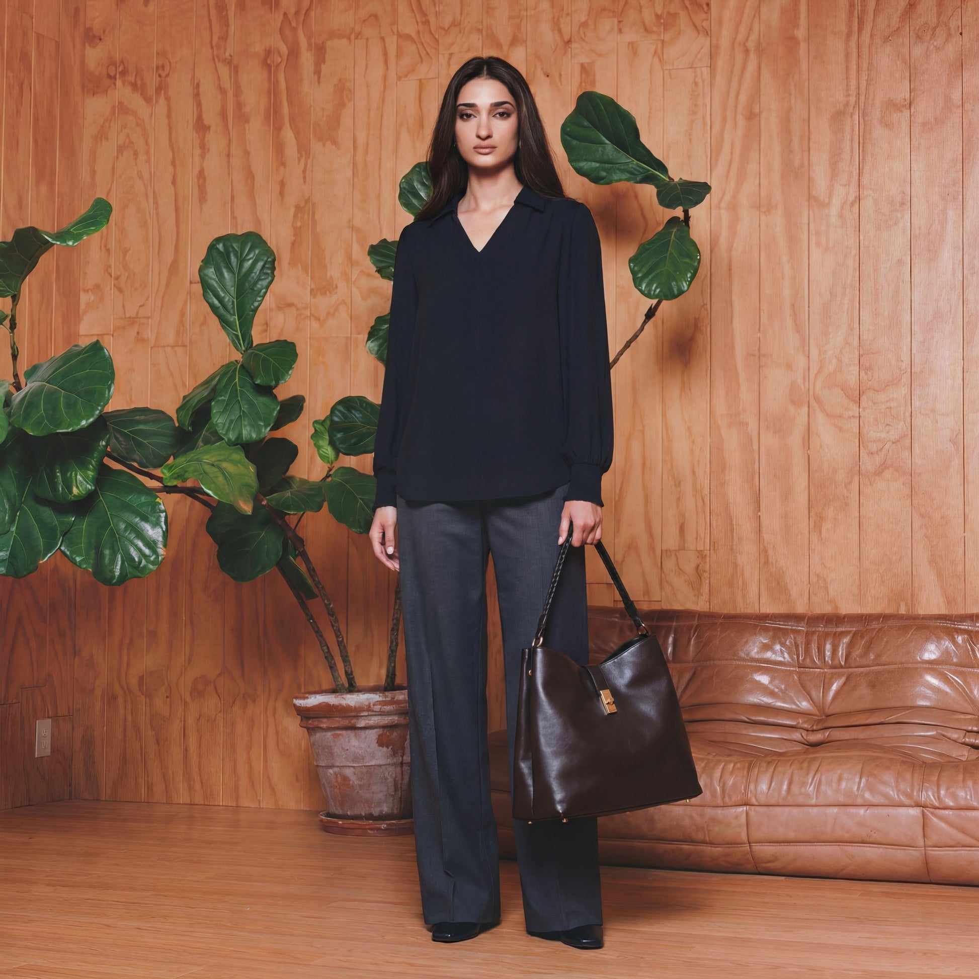 Woman holding a black handbag in a room with wooden walls and a brown leather couch.