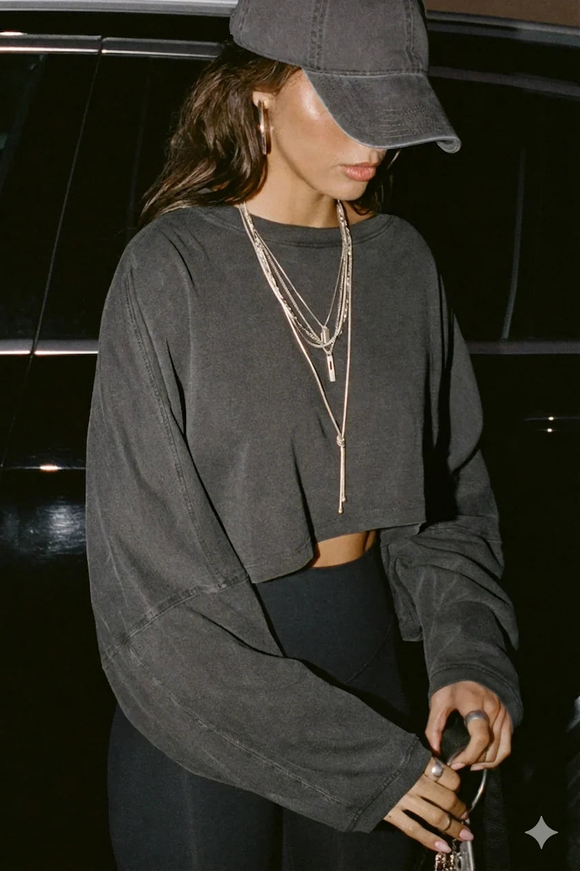 Person wearing a dark grey crop top with layered necklaces in front of a black car.
