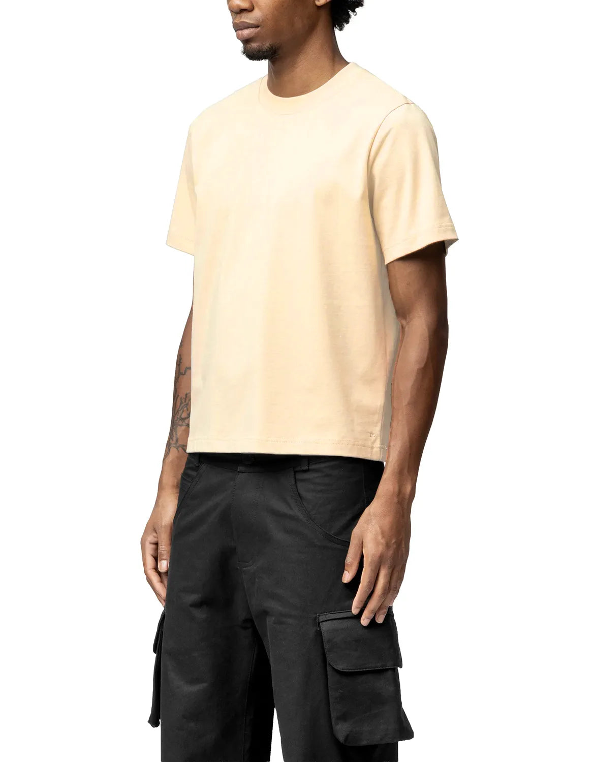 Man wearing a beige t-shirt and black cargo pants on a white background