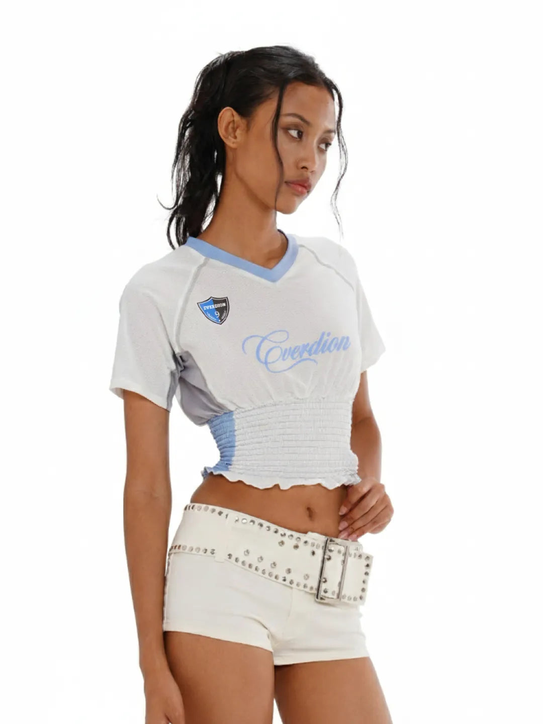Woman wearing a white sports jersey with blue accents and white shorts on a white background