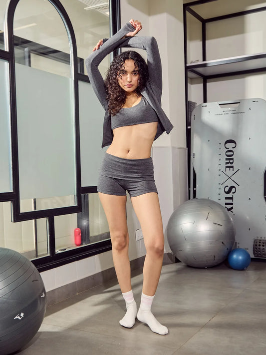 Woman in grey athletic wear stretching in a gym setting with exercise balls and equipment.