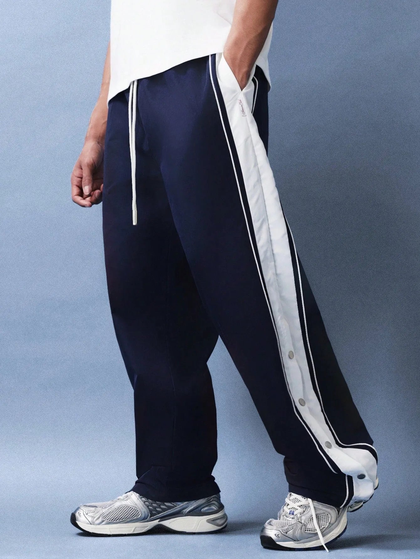 Navy track pants with white stripes worn by a person on a grey background