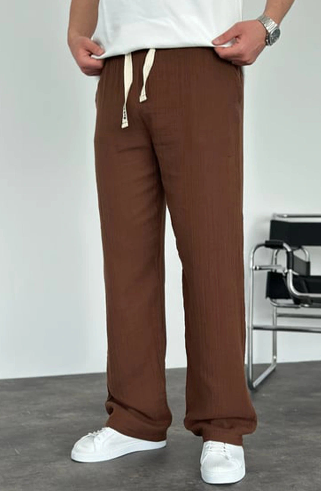 Person wearing brown pants and white shoes in a minimalistic setting
