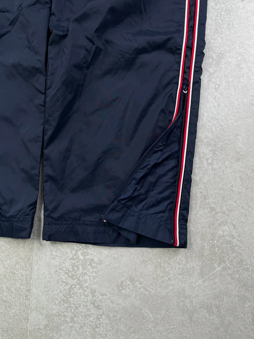 Navy track pants with a red stripe and brand logo on a grey background