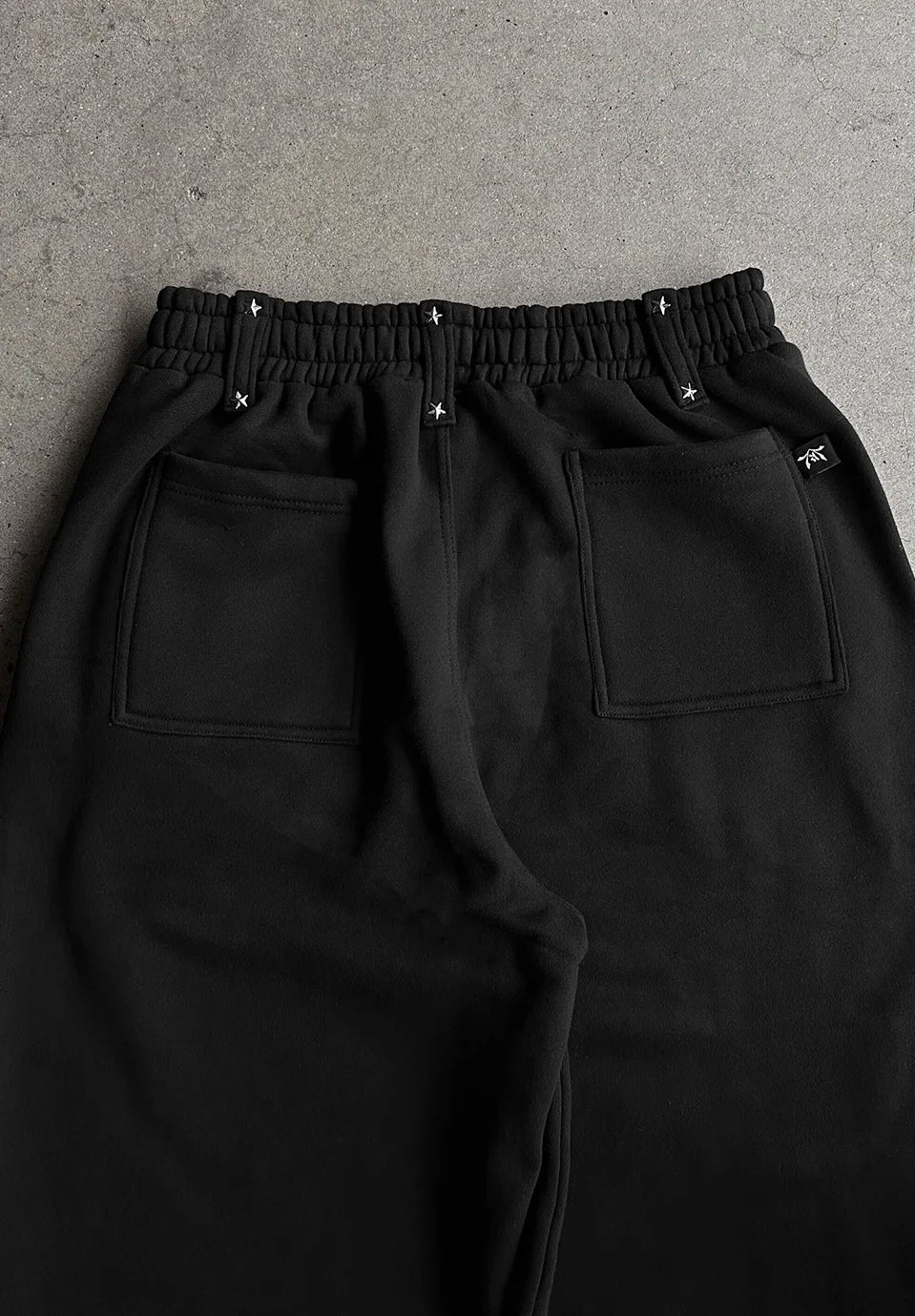 Black sweatpants with an elastic waistband, two large patch pockets, and small silver star details