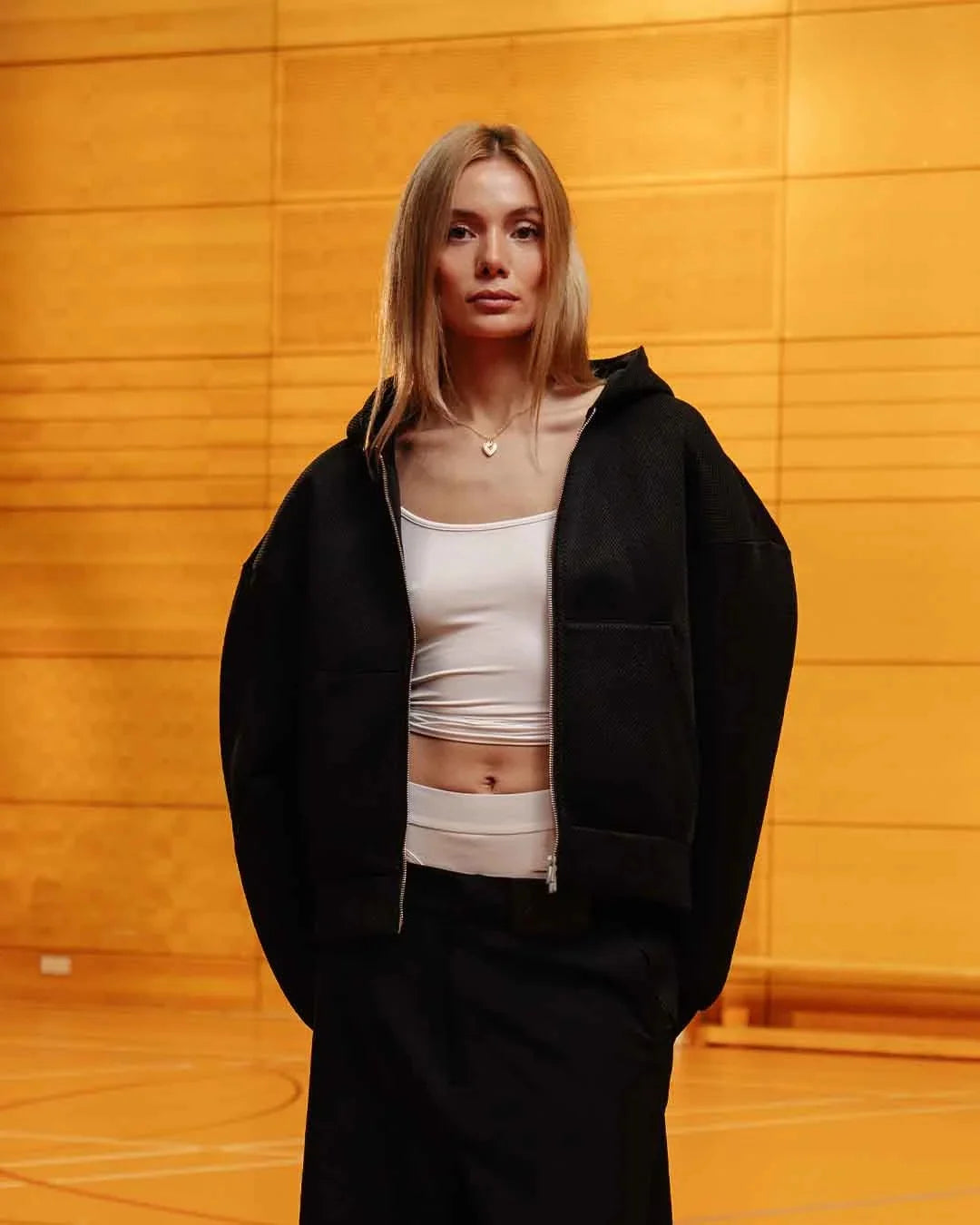 Person wearing a black jacket over a white top against an orange wall.