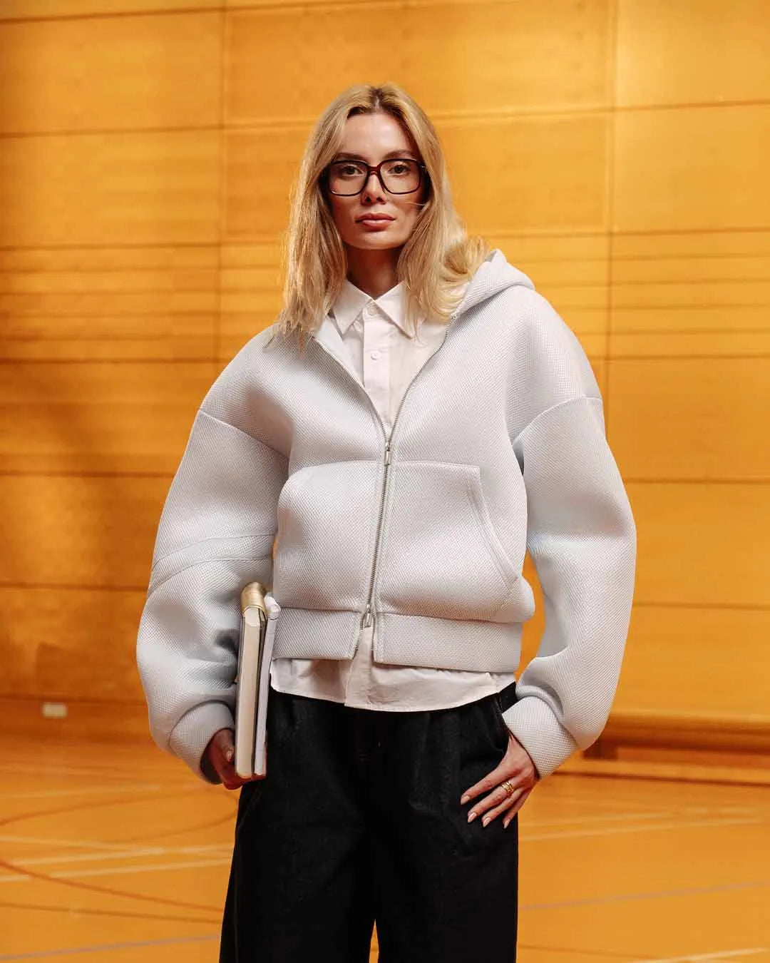 Person wearing a white hoodie and black pants against a wooden background