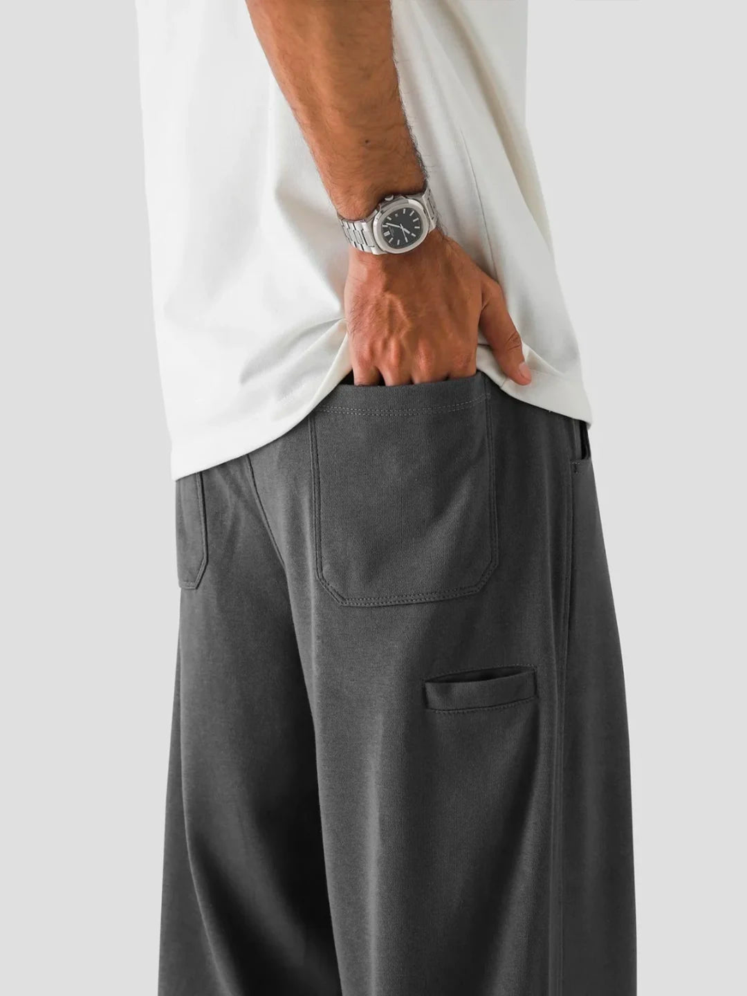 Person wearing grey pants and a white shirt with a watch on a light grey background
