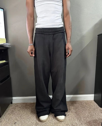 A person wearing black baggy sweatpants, a white tank top, and white sneakers