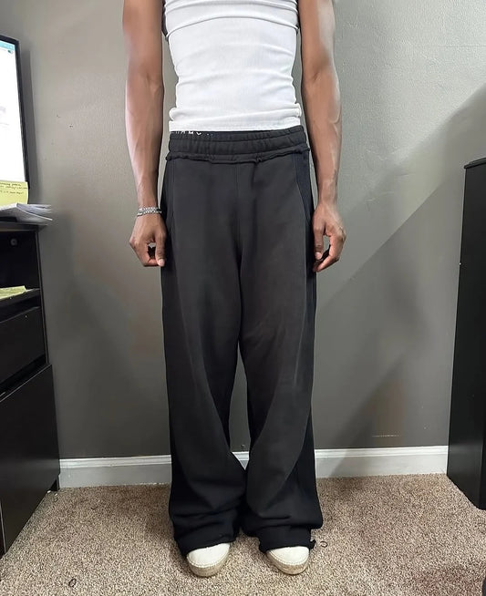 A person wearing black baggy sweatpants, a white tank top, and white sneakers