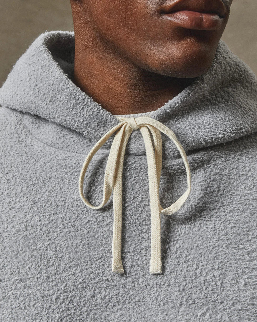 Close-up of a person wearing a gray fleece hoodie with a beige drawstring.