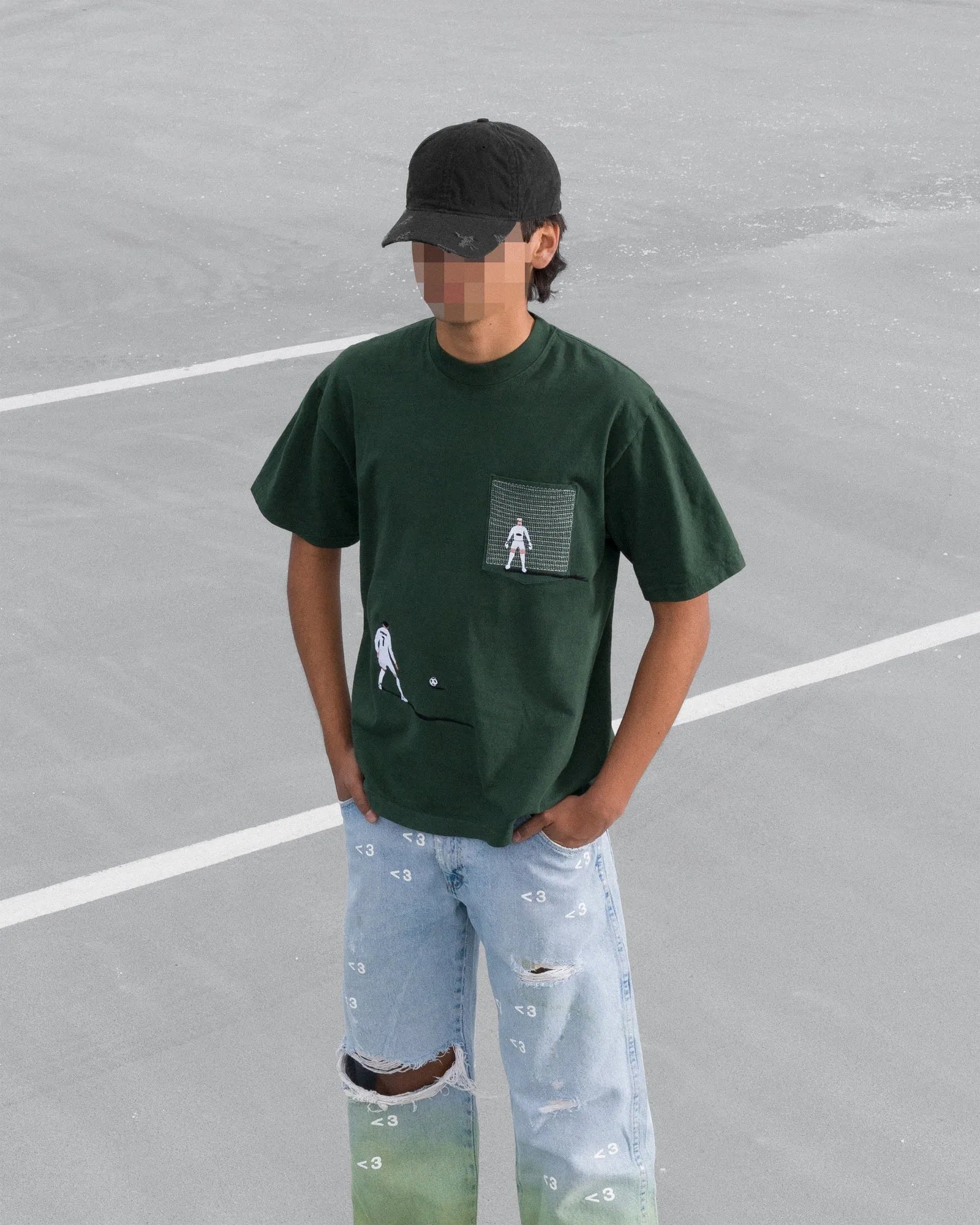 Person wearing a dark green t-shirt with a graphic design and light blue jeans on a grey surface.