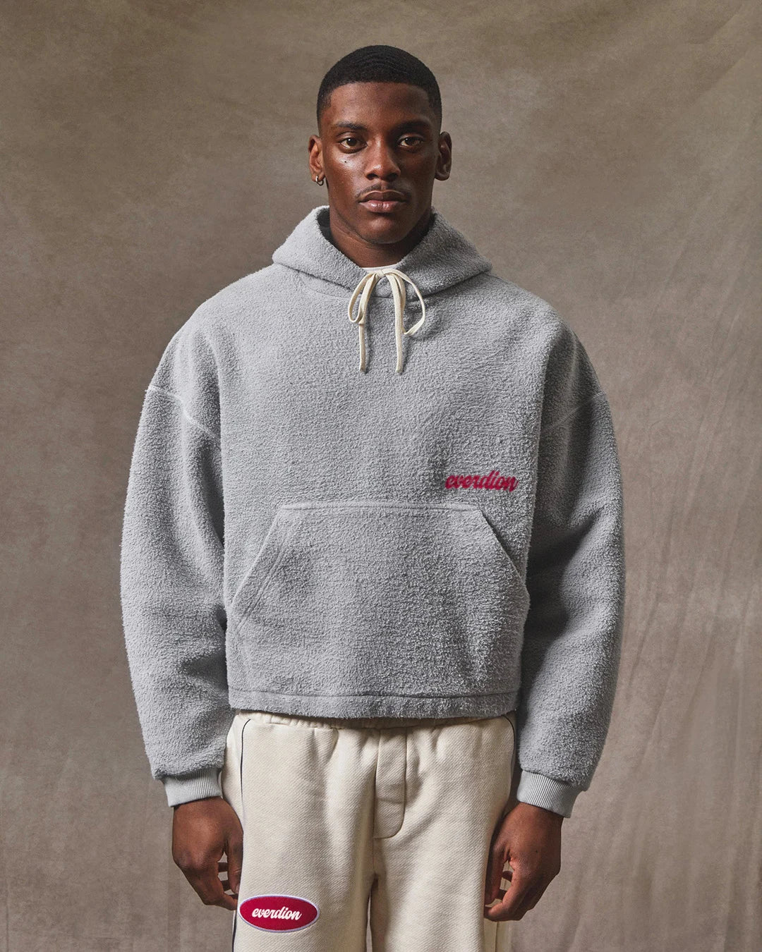 Person wearing a gray hoodie with a brand logo on a brown background