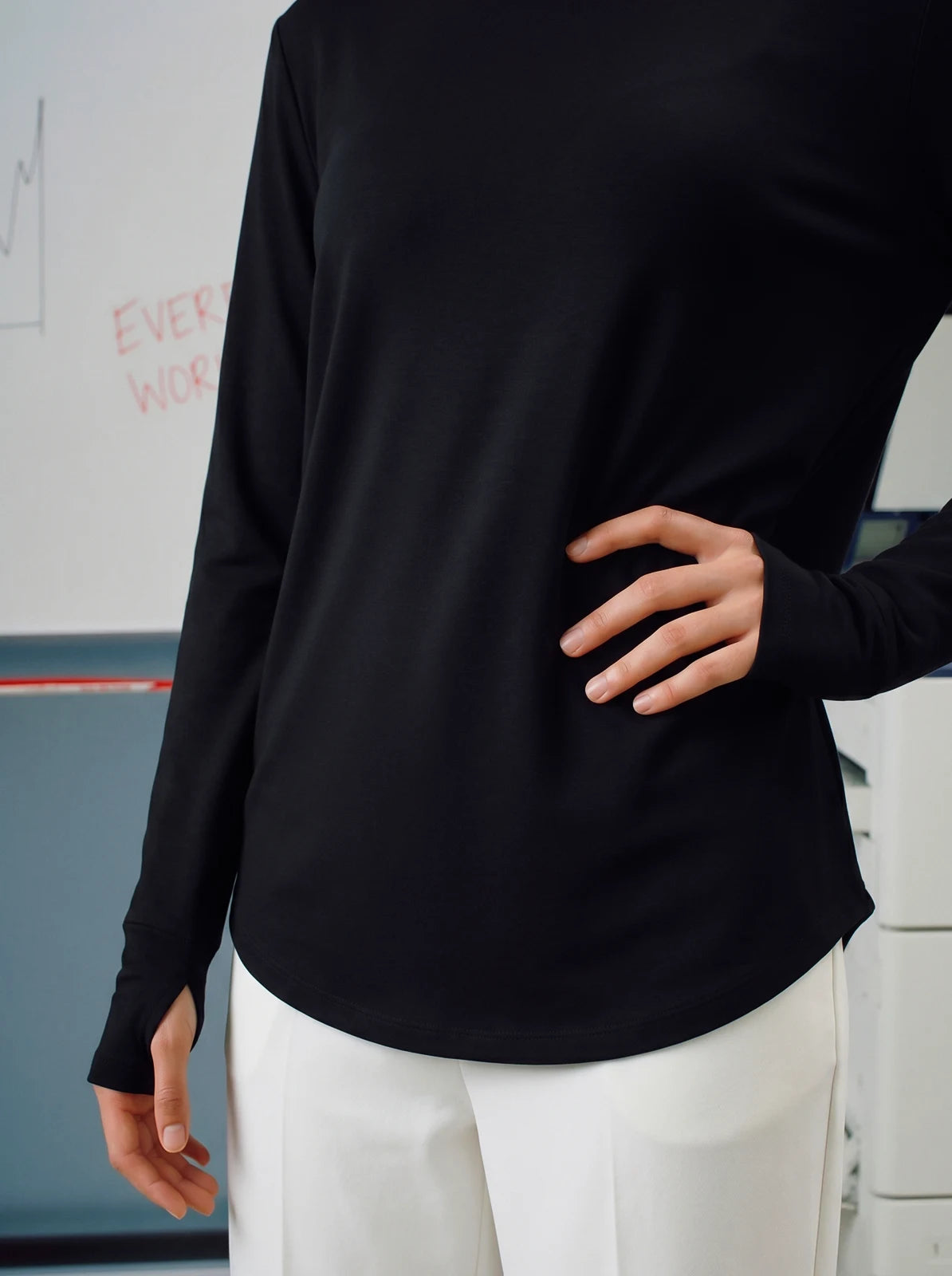 Person wearing a black long-sleeve top and white pants in an indoor setting.