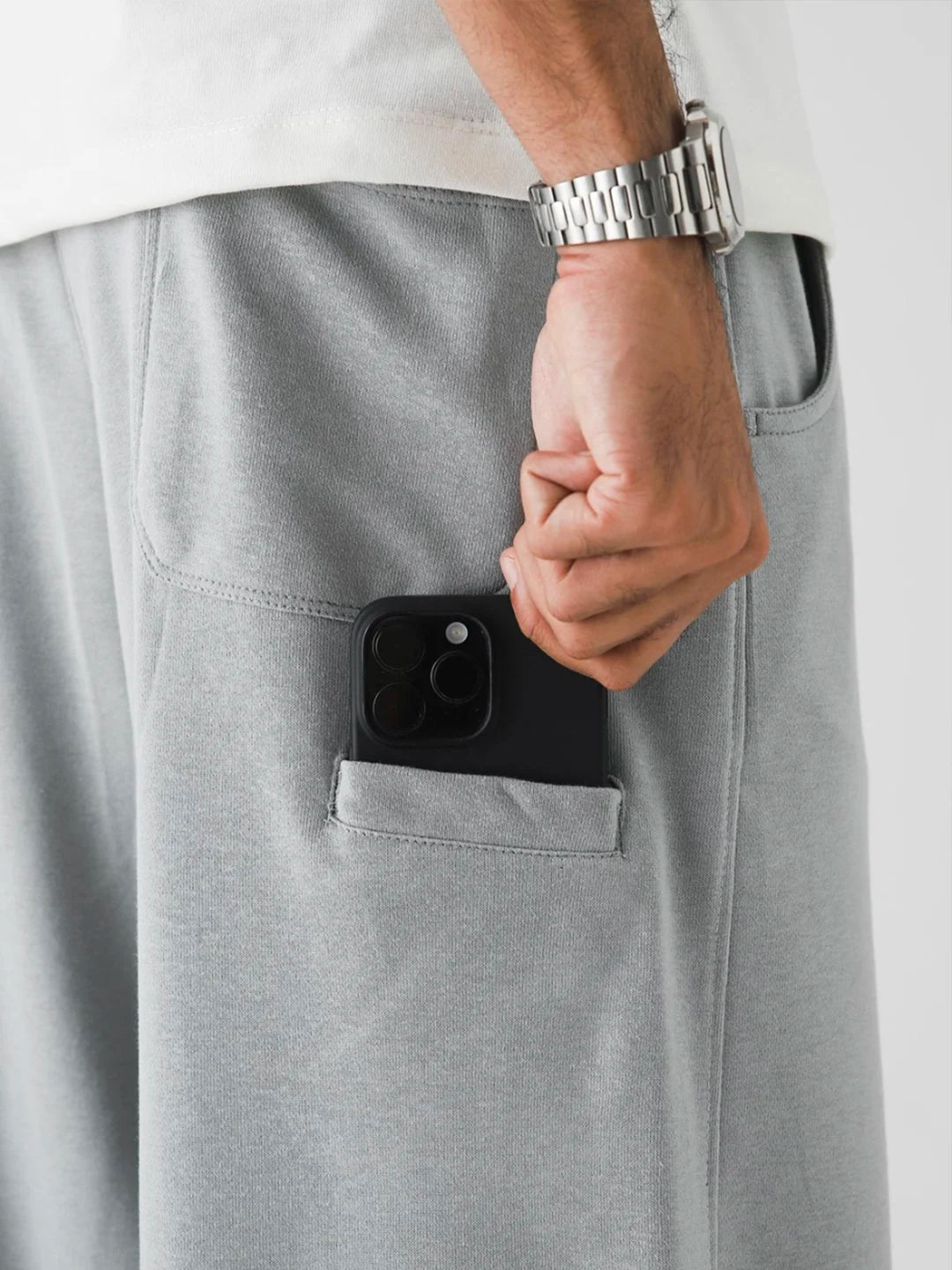 Person wearing grey pants with a phone in the pocket against a light background
