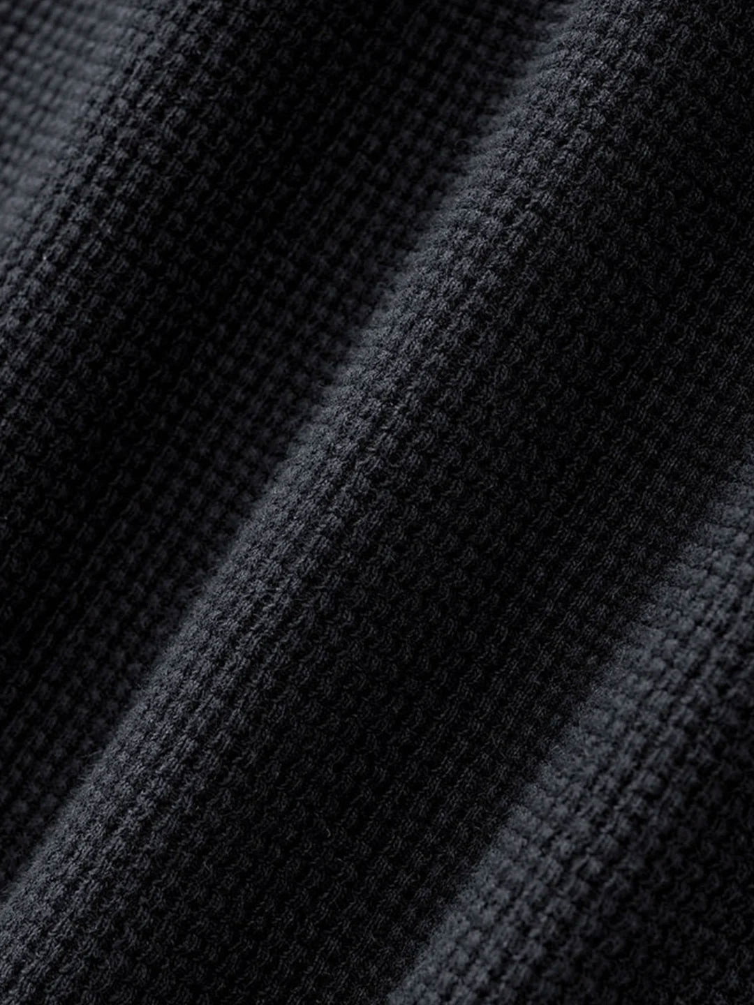 Close-up of a dark charcoal grey waffle knit fabric texture with diagonal folds.