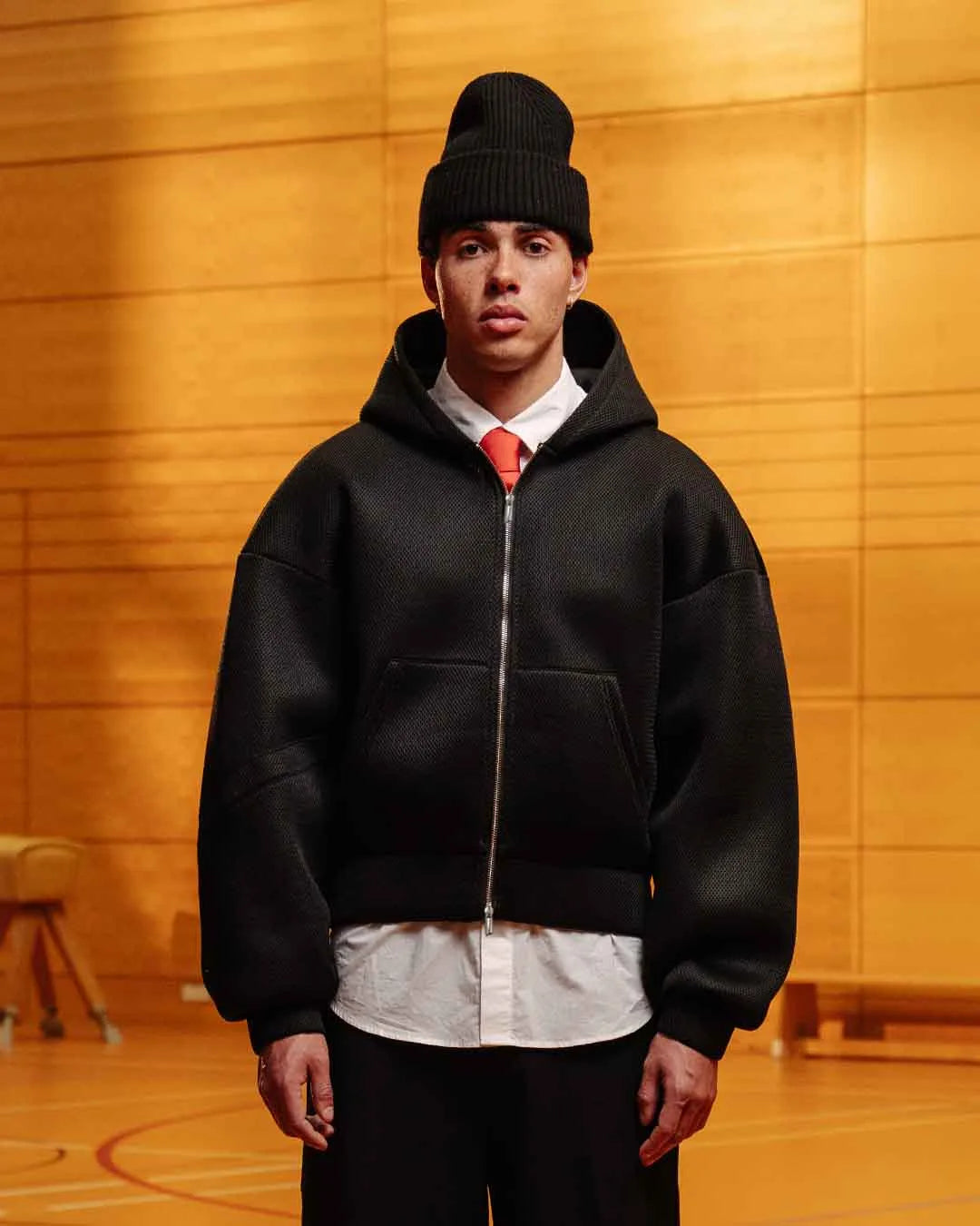 Person wearing a black hoodie and beanie in an indoor setting with wooden walls.