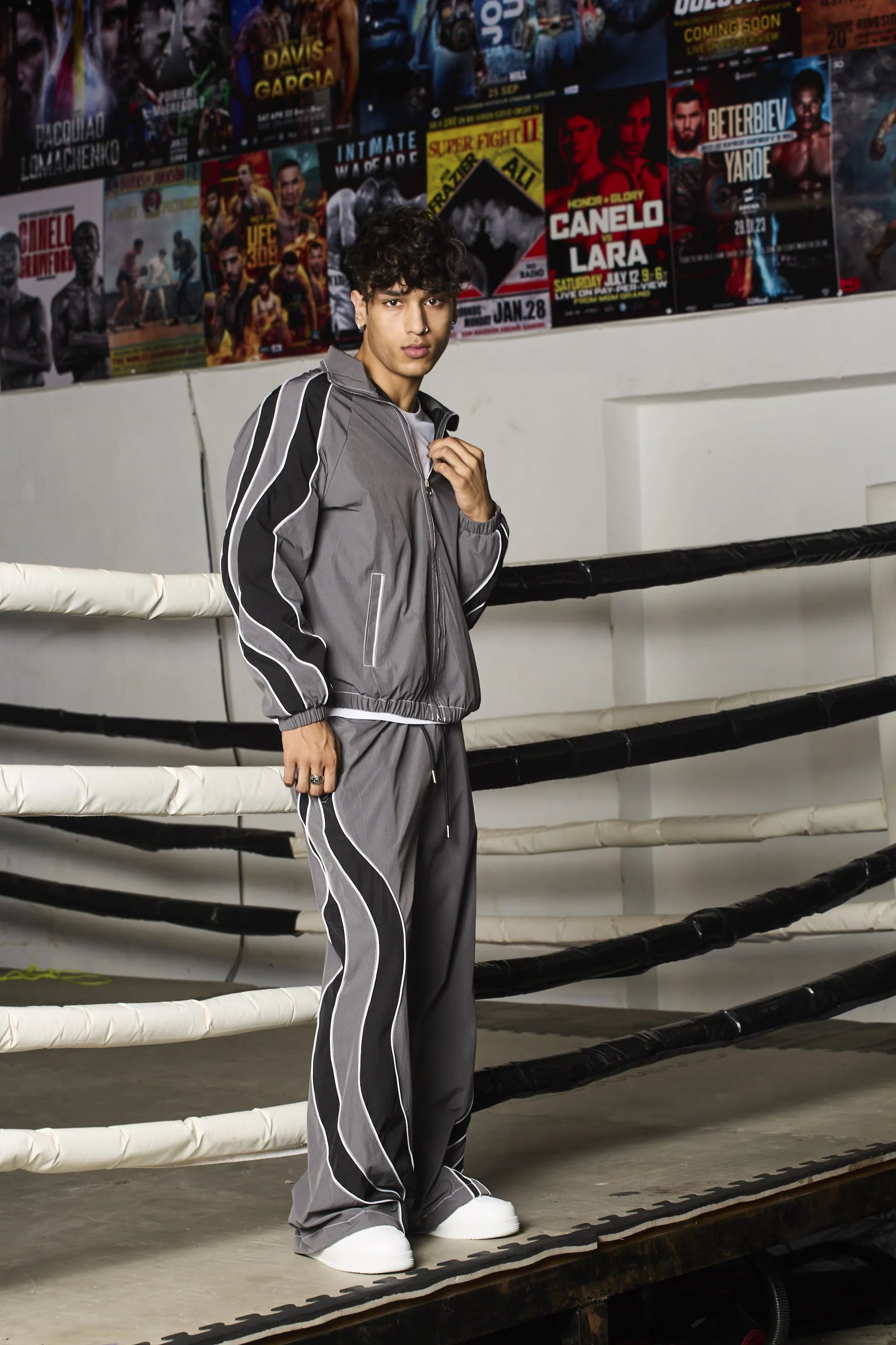 Person wearing a grey tracksuit with white stripes in a boxing ring setting.